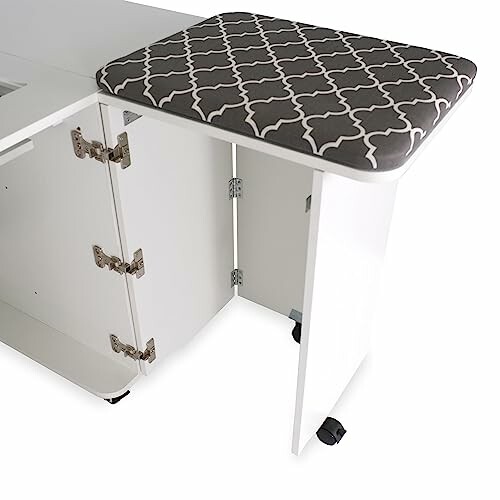 Folding sewing table with cushioned top and storage cabinet.